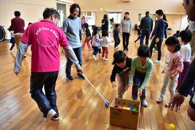 指導者が段ボールに紐をつけて引っ張りその中にボールを片付けている子供たちの写真