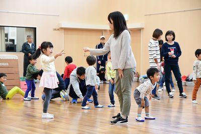 女の子と、お母さんがじゃんけんをしており、その後ろでは、子供たちが笑顔で話をしたり、座っている写真