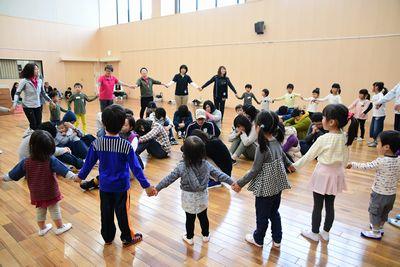 子供や、スタッフたちが手をつなぎ大きな輪を作り、輪の中で座って顔を伏せたり、手で顔を覆う男女の写真