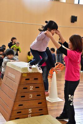 跳び箱の上から大人と手をつないでジャンプしている小さな女の子の写真