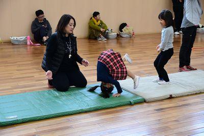 体育マットの上で前回りをする女の子と、その横で危なくないように見守る女性の写真