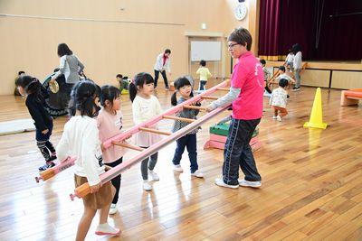 ピンク色のシャツを着た女性スタッフと、女の子4人が一緒に木のはしごを運んでいる写真