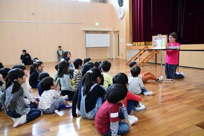 床に座っている子供たちの前で、紙芝居の読み聞かせをする女性スタッフの写真