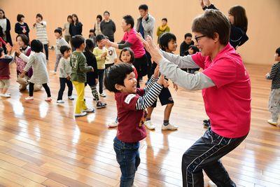 ピンクのシャツを着た女性と両手でハイタッチをする男の子と、その奥でもスタッフとハイタッチをする子供たちの写真