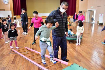 斜めに置かれたはしごの上をお父さんと手をつないで渡っている男の子の写真