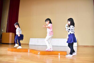 低い木製の平均台をバランスを取りながら渡っている子供たちの写真