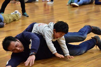 横の体制に寝転んだお父さんの上に乗っかっている男の子の写真