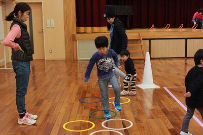 床に並べられたリングを片足でジャンプして進んでいる男の子の写真