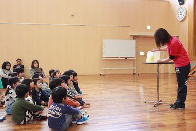 スタッフが読んでいる本を床に座ってじっと見聞きしている子供たちの写真