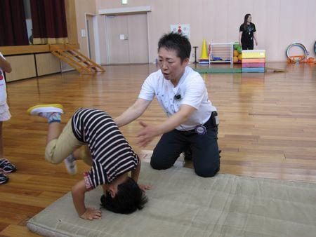 男の子が体育マットに頭と両手をついて前転をしようとしており、スタッフの女性が両手を前に出して補助をしようとしている写真