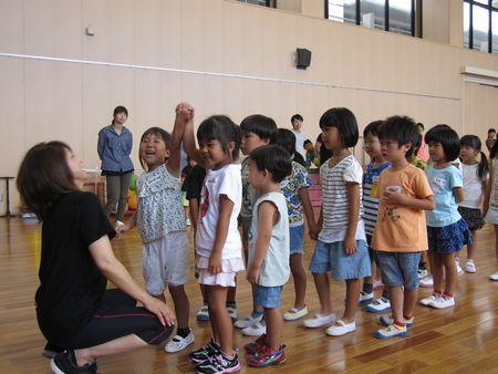 子ども達が2人1組で手をつないでスタッフの女性の前に1列に並んでおり、一番先頭の女の子2人がつないだ手を挙げて笑顔で笑っている写真