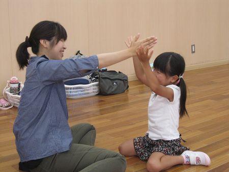 女の子とお母さんが向き合って座っており、女の子が頭の上でお母さんの手が降り落ちてこないように止めようと両手でお母さんの手を挟もうとしている写真