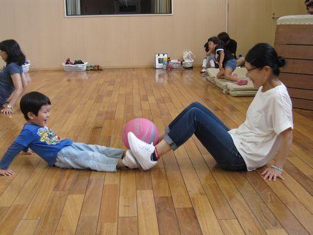 男の子とお母さんが向かい合って座っており、伸ばした両足でピンク色のボールを掴んでいる写真