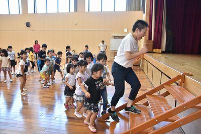 舞台の階段を上る、短髪の女性に続く子供たちの写真