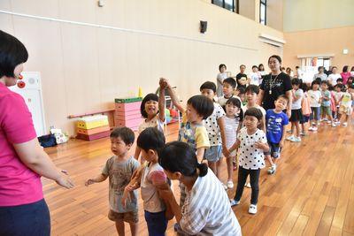 ピンクのシャツを着た女性の前に、2人組になり手をつないで並ぶ子供たちの写真