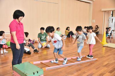 跳び箱にはしごを片方立てかけて、その上を子ども達が歩いており、スタッフの方が側で見守っている写真