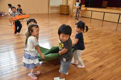 体育マットを半分に折って、4人の小さい子ども達が力を合わせて運んでいる写真