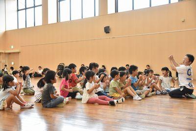 スタッフが正座をして床に座っており、子ども達が集まって一緒に手遊びをしている写真