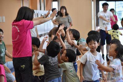 スタッフの女性が両手を広げて手を伸ばしており、子ども達が集まって来て、ジャンプしてスタッフの手にハイタッチをしている写真