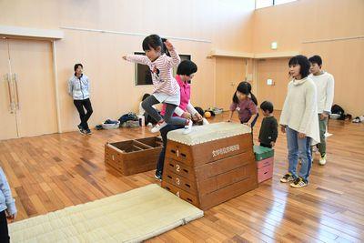 4段の跳び箱の上からジャンプして飛び降りる女の子と、その横で見ているお母さんや女性スタッフの写真