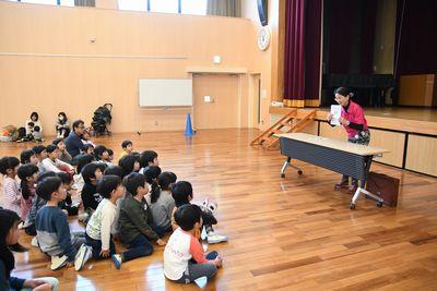 床に座る子供たちの前で、読み聞かせをする女性スタッフの写真