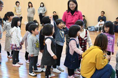 2人組で手をつないで列を作る子供たちが、列の真ん中あたりでつないだ手を高く上げて返事をしている女の子2人組を見ている写真