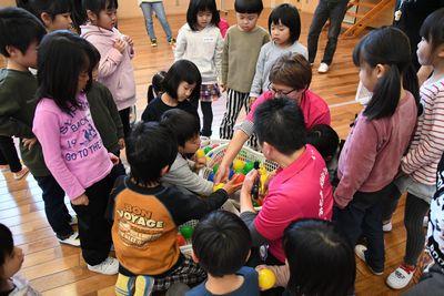 かごに入ったカラフルなボールの周りに集まる子供たちと女性スタッフの写真