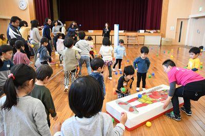 倒れた赤鬼のマットのようなものを起こす女性スタッフと、その周りで見ている子供たちの写真