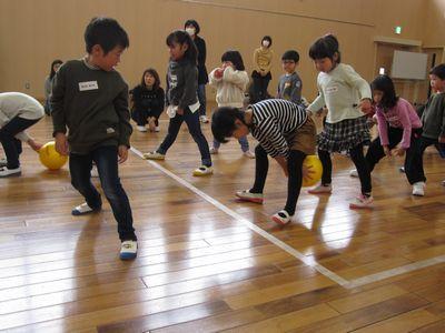 2列に並んでいる子供たちが、両足の間から、次の人にボールを渡している写真