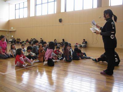 出席カードを持って名前を呼ぶ女性スタッフと、座っている子供たちの中で、1人の女の子が手をあげている写真