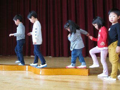細い木の上を順番にわたる子供たちの写真
