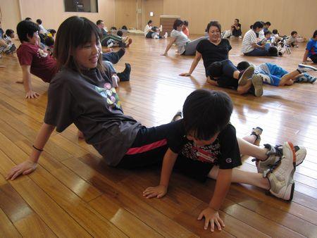 お母さんが両手を後ろについて足を交差して伸ばして座り、交差した足の間に男の子が体を半分入れている写真