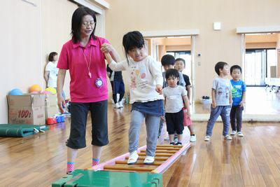 はしごを斜めに床に置いてその上を歩いている子供たちの写真