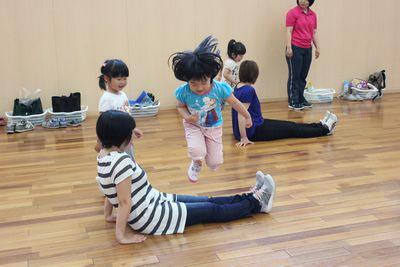 お母さんが足を延ばして座りその上を子供がジャンプしている写真