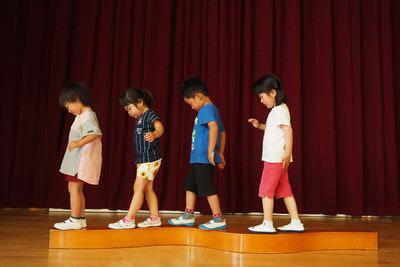 平均台のような木の上を落ちないように慎重に歩いている4人の子供たちの写真