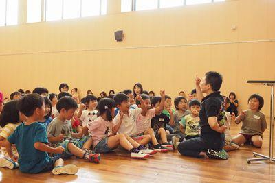 指導者の周りに集まって手遊びをしている子供たちの写真
