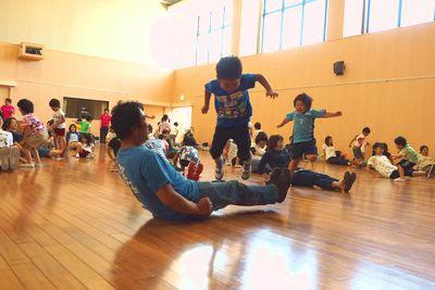 お父さんが足を延ばしその上を子供がジャンプしている写真