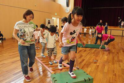 はしごを斜めに置いてその上を渡っている子供たちの写真