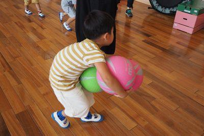 ボールを両手いっぱいに3個持って運ぼうとしている男の子の写真