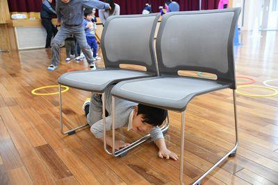 二つ並べられた椅子の下を男の子がくぐり抜けようとしている写真