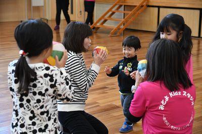 中央にお母さんが座っていて紙風船を膨らませていて、周りにいる子どもたちも紙風船を膨らませようとしている写真