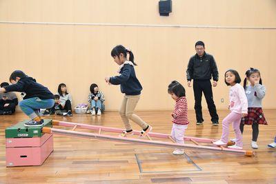 跳び箱に梯子が横になって立てかけられていて、その上を子どもたちが歩いている写真