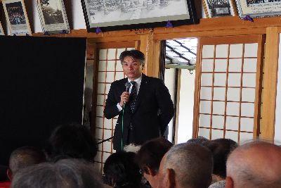 スーツを着た山下 昭史市長が部屋の入口付近に立ち右手にマイクを持って話をしている写真
