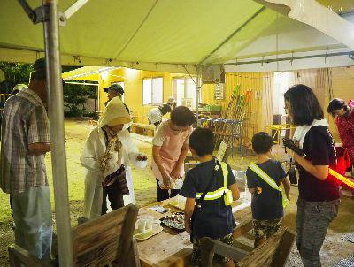建物にはライトが付けられ、テントの中で子供2人が食事を受け取ろうとしている写真