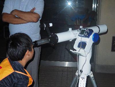 オレンジのゼッケンをはめた男の子が望遠鏡を覗いている写真