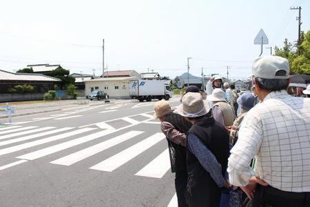 横断歩道の前で止まり警察官の指示を聞いている高齢者の皆さんの写真