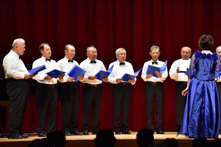 指揮者の豊岡 真弓さんから向かって左側の男性コーラスメンバーが歌を歌っている写真