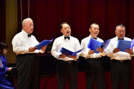男性4名が大きな口を開けて歌を歌っている写真