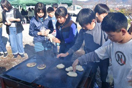 外の鉄板で生地を焼いている子供たちの写真