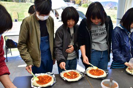 生地にピザソースを塗っている子供たちの写真